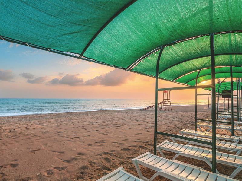 Plage avec chaises longues sous des parasols verts au coucher du soleil