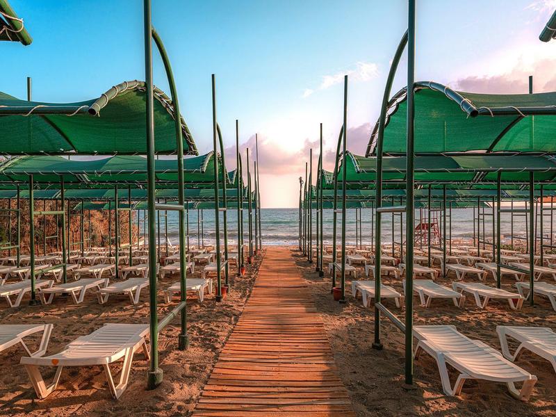 Coucher de soleil sur la plage avec passerelle en bois vide et rangées de parasols verts