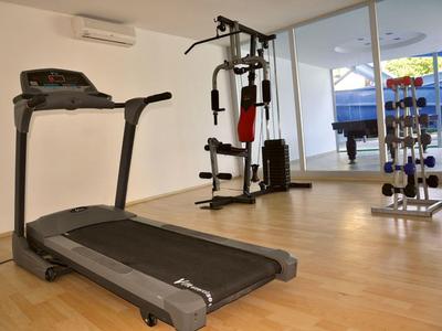 Equipos de gimnasio modernos como cinta de correr y máquina de cables en sala luminosa con suelo de madera.