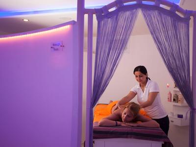 Donna che riceve un massaggio in una stanza benessere rilassante con tende viola e luce soffusa