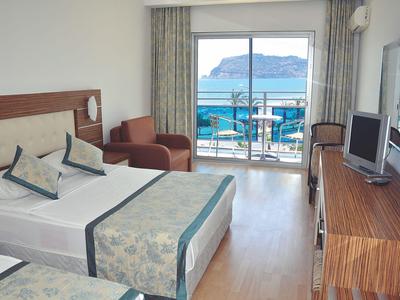 Habitación de hotel con dos camas, balcón y vista al mar y una isla rocosa.