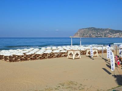 Spiaggia con file di ombrelloni e lettini, mare sullo sfondo con colline.