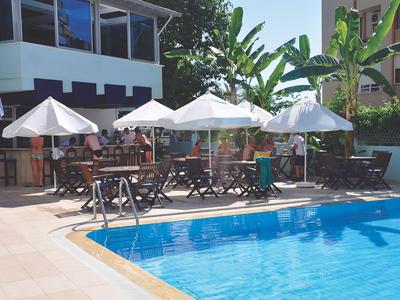 Zona de piscina con sombrillas y tumbonas junto a un hotel con plantas tropicales.