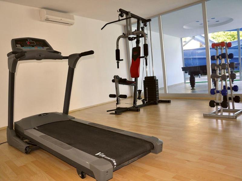 Palestra moderna con tapis roulant, attrezzi multifunzione e pesi davanti a grandi finestre.