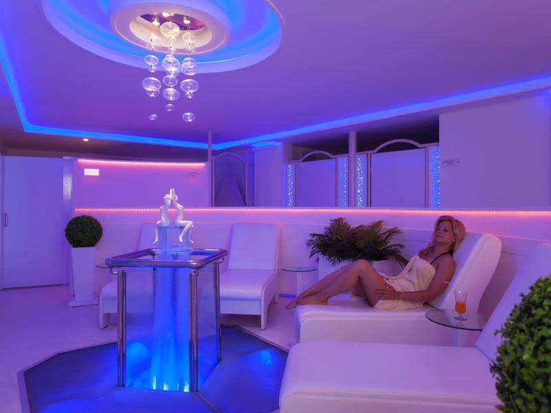 Donna rilassata sdraiata in una stanza spa moderna con illuminazione blu-viola.