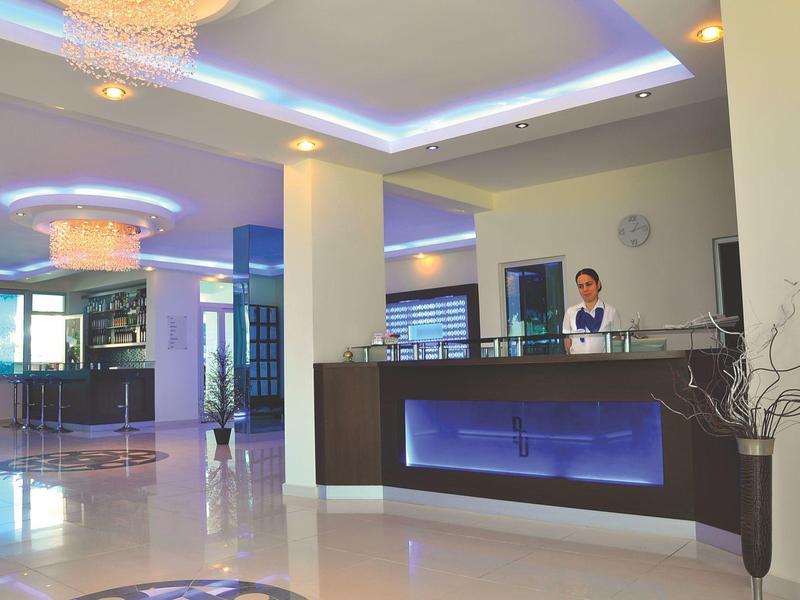 Area lobby moderna con reception, pavimento chiaro e luci a soffitto illuminate.