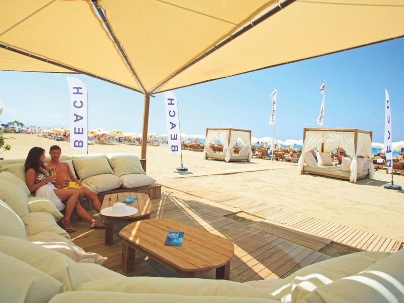 Coppia seduta su comodi divani sotto una tenda da sole in spiaggia con vista su lettini.