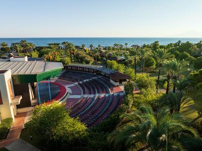 Openluchttheater met rode zitplaatsen, omgeven door palmbomen met uitzicht op zee.