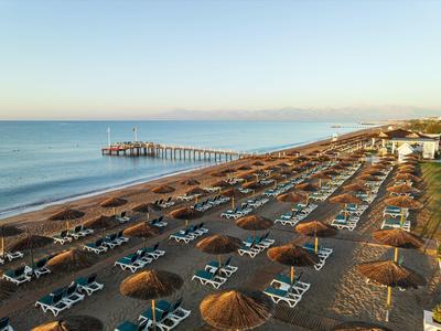 Dlouhá písečná pláž s řadami lehátek a slunečníků a dlouhý mol vstupující do moře.