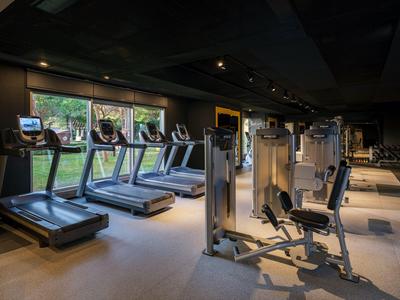 Moderne sportschool met loopbanden en krachtapparaten bij ramen met uitzicht op groen.