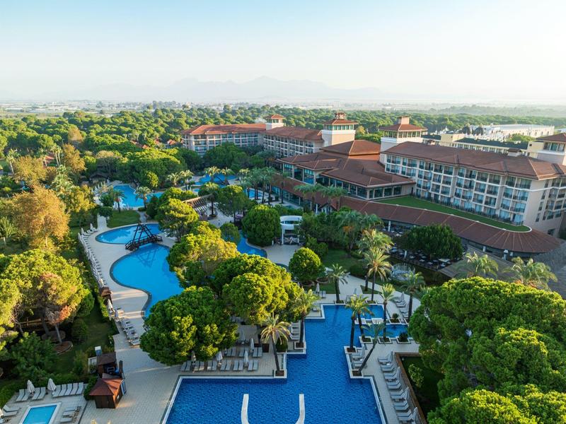 Velký hotelový komplex s několika bazény a bohatou zelení ve slunné krajině