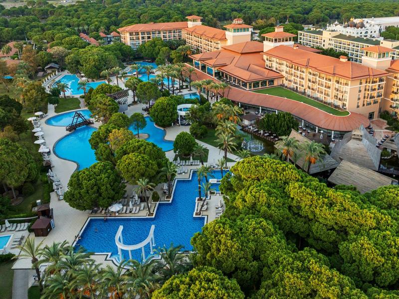 Letecký pohled na resort s několika bazény obklopenými tropickými stromy a velkými budovami.