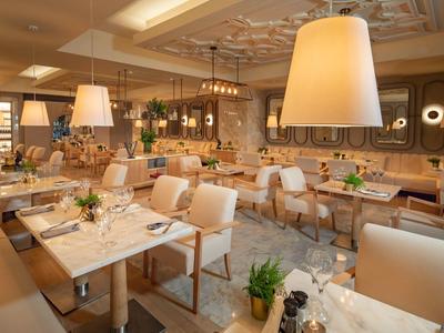 Modern eingerichteter Restaurantraum mit hellen Sesseln, Holztischen und großen Pendelleuchten.