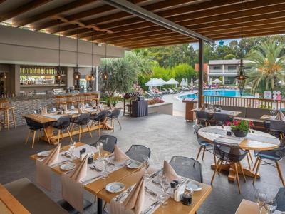Moderner Außenbereich eines Restaurants mit gedeckten Tischen, Holzmöbeln und Poolblick.