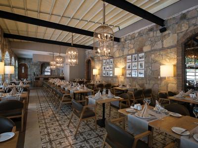 Elegantes Restaurant mit grauen Steinwänden, Holzvertäfelung, Kronleuchtern und gedeckten Holztischen.