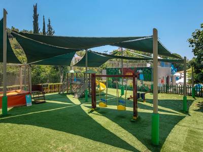 Kinderspielplatz mit Klettergerüst, grünem Kunstrasen und schattenspendernden Sonnensegeln.
