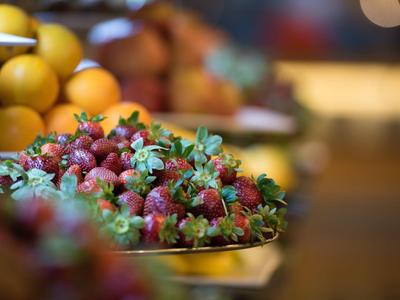 Frische rote Erdbeeren mit grünen Blättern auf einem Marktstand, unscharfer Hintergrund mit Orangen.