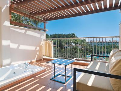 Helle Terrasse mit Holzpergola, Whirlwanne, Sofa und Tisch mit Blick auf Meer und grüne Hügel.
