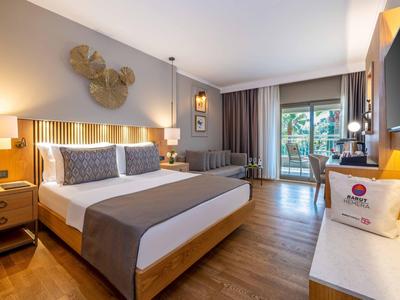 Modernes Hotelzimmer mit Doppelbett, Sofa, Holzboden und Zugang zu einem Balkon mit Gartenblick.