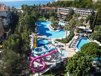 Großer Hotelpool mit Wasserrutschen, umgeben von Liegestühlen und grünen Bäumen, nahe am Meer.