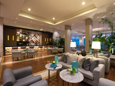 Nowoczesny salon hotelowy z wygodnymi fotelami, okrągłymi stolikami i stylowym oświetleniem.