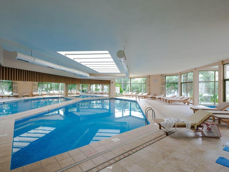 Piscina interna riscaldata con lettini e grandi finestre in un hotel per vacanze.