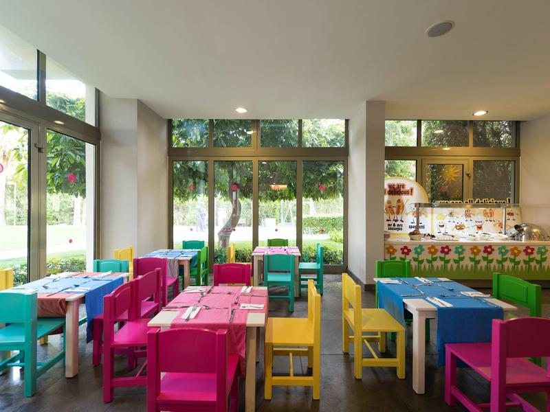 Sala giochi colorata per bambini con piccoli tavoli e sedie accanto a grandi finestre.