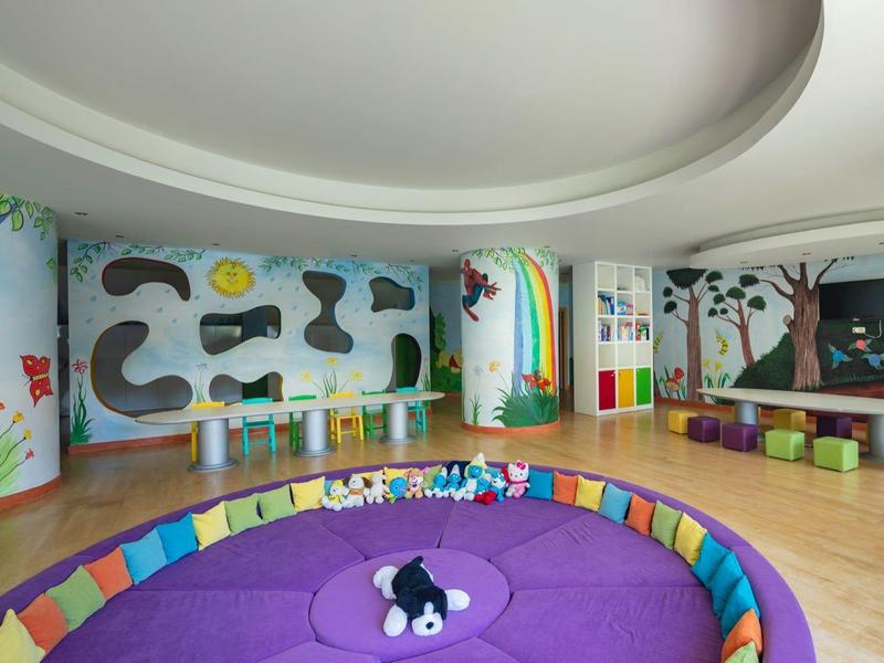 Camera interna colorata con muro arcobaleno, cuscini e area bambini in un hotel.