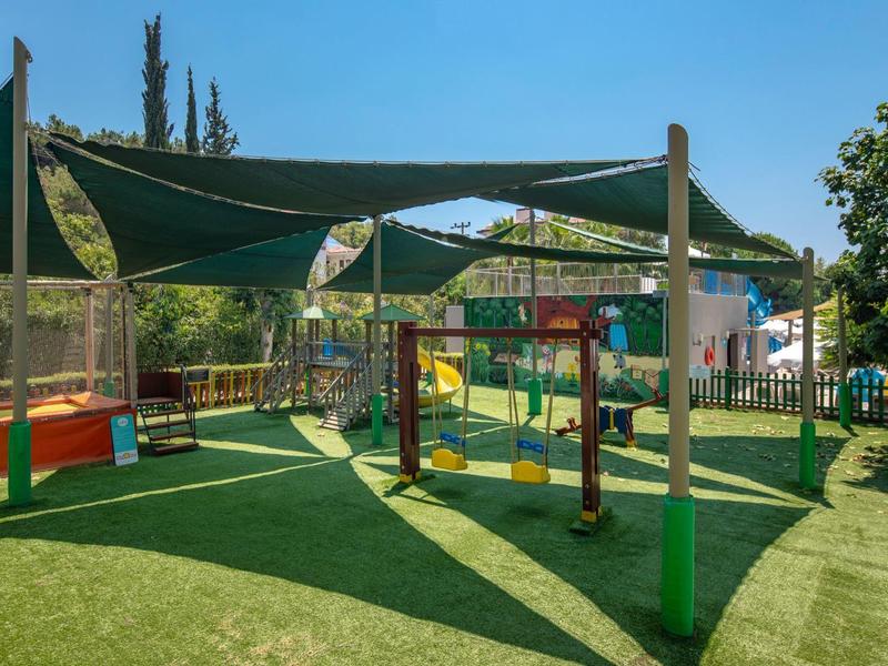 Parco giochi ombreggiato con struttura per arrampicata e scivoli su prato artificiale verde