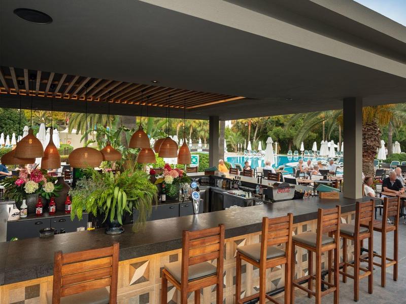 Bar aperta con sgabelli di legno con vista su una piscina di un hotel.