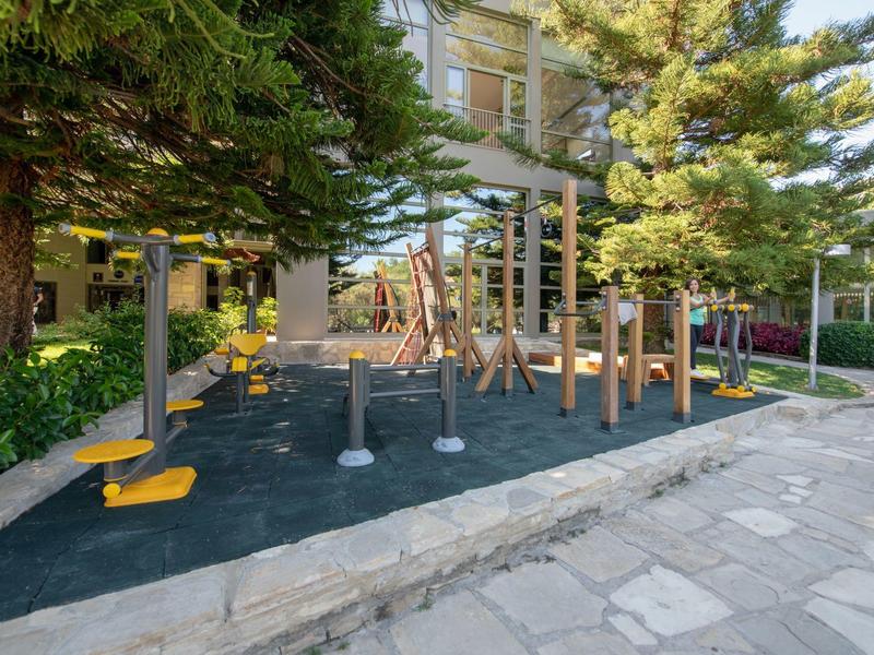 Un parco giochi moderno all'aperto con altalene e strutture da arrampicata accanto a un edificio dell'hotel e alberi.