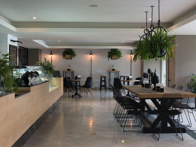 Area pranzo moderna con tavoli in legno, sedie nere e piante sospese in un hotel.