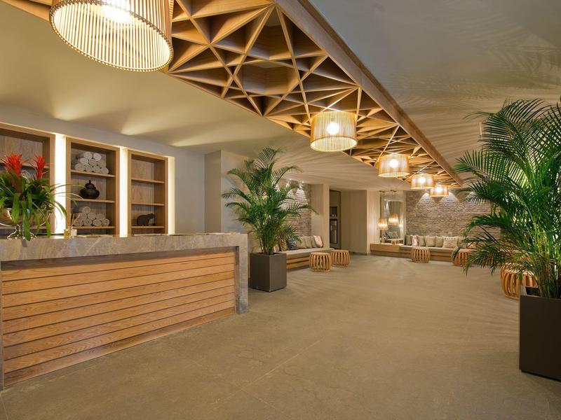 Ampia hall dell'hotel con banco reception, elementi in legno e piante verdi in vasi moderni.