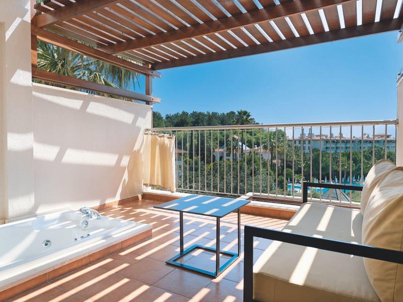 Balcone con vasca idromassaggio, divano e tavolo con vista sul mare sotto una pergola in legno.