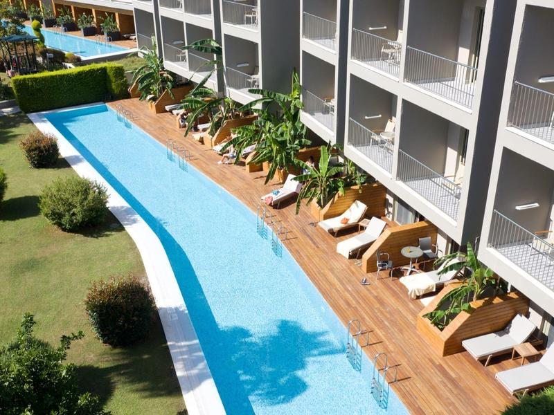 Hotel con una lunga piscina, lettini e balconi accanto a un'area giardino.