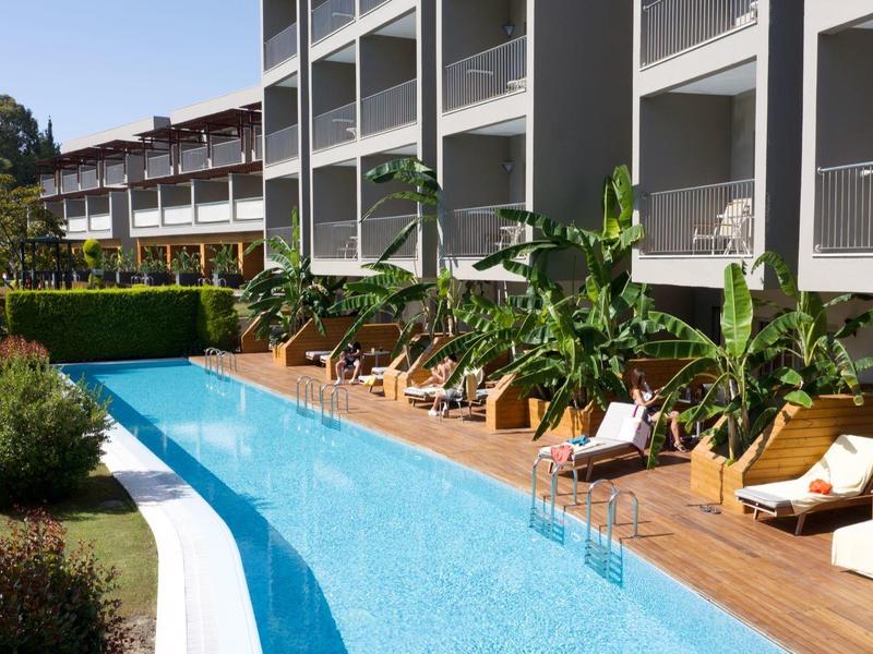Piscina moderna dell'hotel con lettini e piante su una terrazza in legno accanto all'edificio.