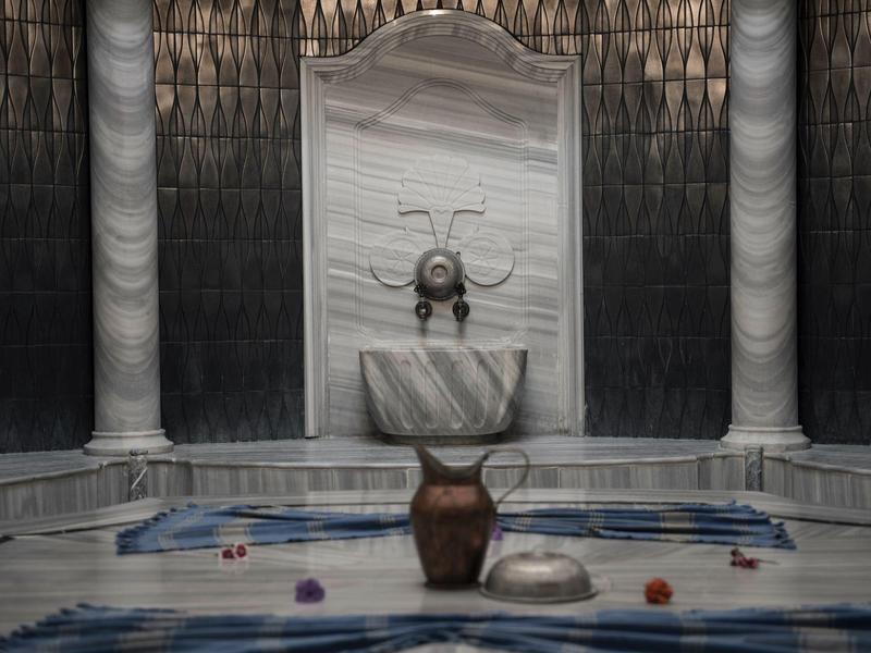 Hammam turco tradizionale con colonne architettoniche, lavabo in marmo e brocca d'acqua.