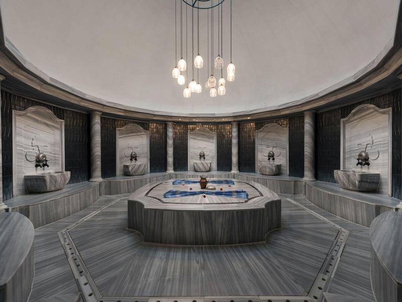 Bagno turco di lusso rotondo con pareti in marmo, lavabo centrale in marmo e lampadario