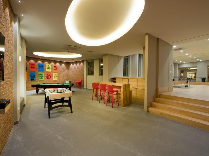 Sala ricreativa moderna con calcio balilla, sgabelli da bar e decorazioni murali colorate.