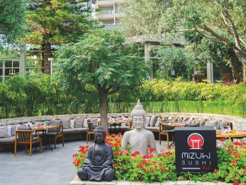 Area esterna di un hotel con posti a sedere e statua di Buddha in un giardino circondato dal verde.