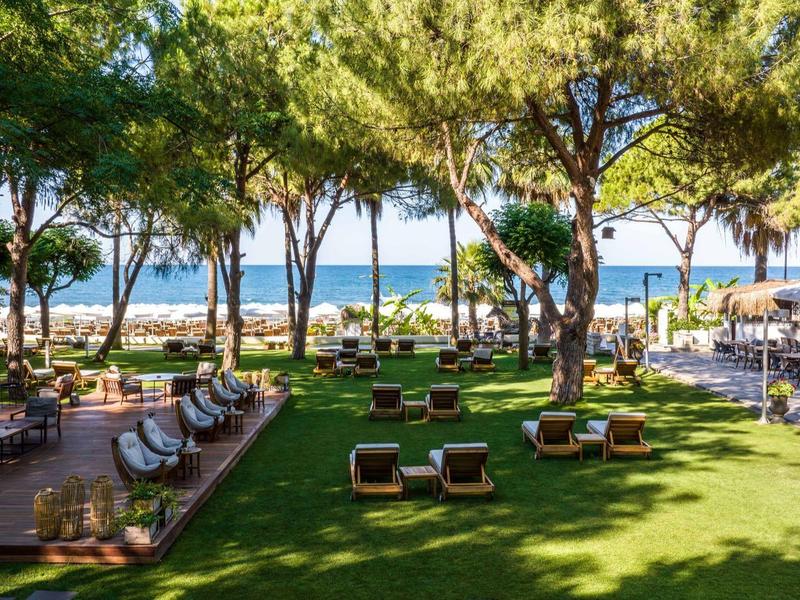 Area giardino verde con posti a sedere, circondata da alberi e vista sul mare