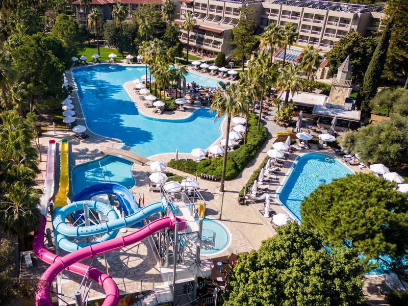 Grande hotel con piscine all'aperto, scivoli d'acqua e lettini circondato da alberi.