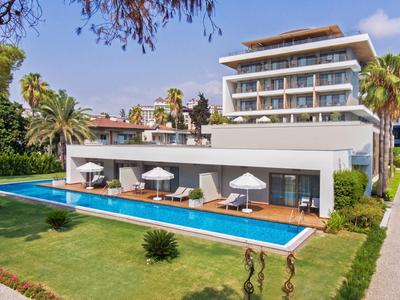 Hotel moderno con piscina, lettini e ombrelloni in un'area giardino verde.