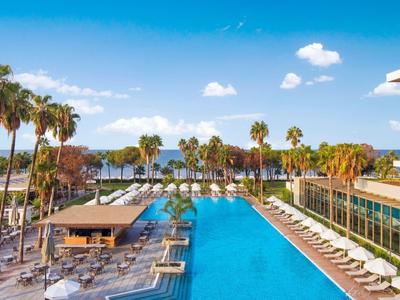 Grande piscina dell'hotel con lettini e palme sotto un cielo azzurro vicino al mare.