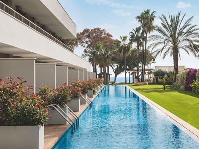 Piscina esterna moderna con area lounge e palme in un hotel vicino al mare.