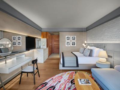 Camera d'hotel moderna e luminosa con letto matrimoniale, scrivania e zona salotto.