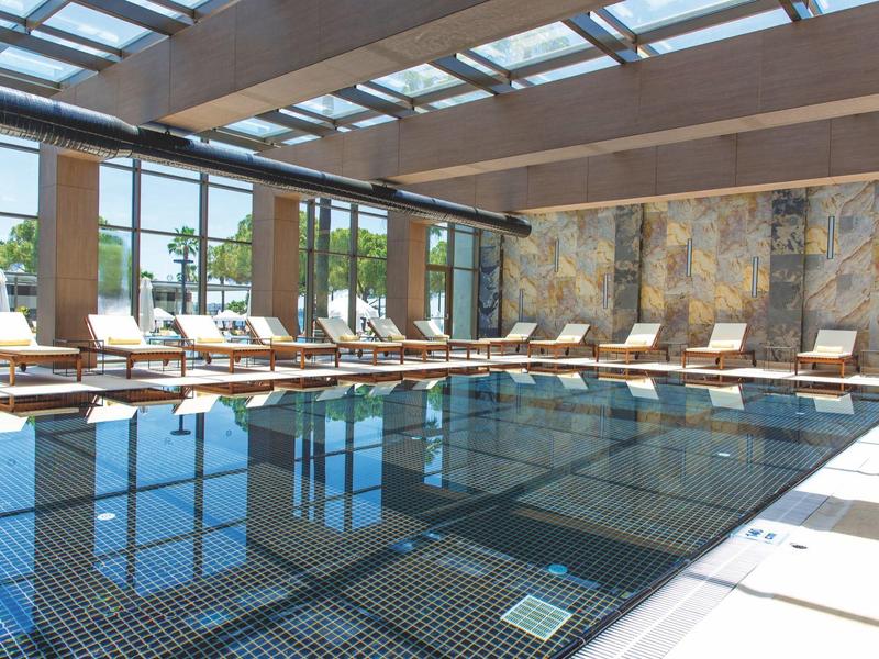 Piscina interna con lettini e grandi finestre che lasciano entrare la luce naturale.