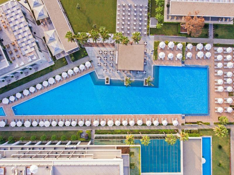 Vista aerea di un hotel moderno con una grande piscina rettangolare e ombrelloni.