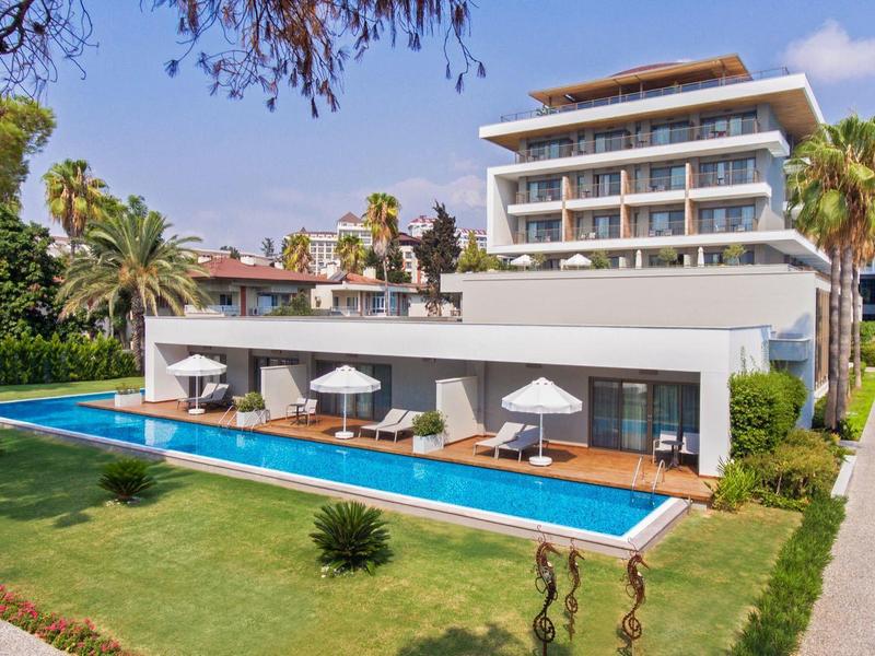 Hotel moderno con piscina, lettini e ombrelloni in un'area giardino verde.