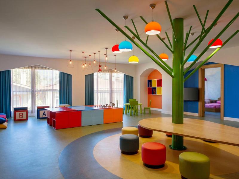 Camera d'hotel luminosa e moderna con mobili colorati e decorazione a forma di albero al centro.